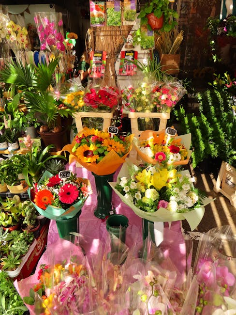 A vibrant display of fresh flower bouquets arranged on a pink cloth-covered table at a florist shop, showcasing a variety of floral arrangements including yellow and orange sunflowers, pink gerbera da