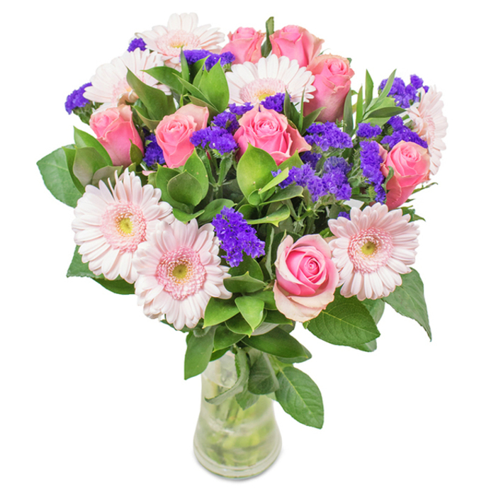 A stunning, gracefully arranged bouquet from Flowers Gipsy Hill stands out in a clear glass vase set before a pristine white background. The arrangement boasts seven to nine medium pink roses-some with petals tightly coiled, others just opening, showing off the classic spiral formation beloved by rose enthusiasts. These are artfully paired with five to seven soft pink gerbera daisies, their large, circular faces and pale centers offering airy brightness. Between the blossoms, clusters of intense purple statice provide striking texture and depth, their bold hue evoking the colourful blooms dotting Gipsy Hill's flower-filled verges and garden squares. Deep, lush greenery forms a luxuriant base, adding contrast and amplifying the sense of freshness and vitality. Visible stems and clear water in the vase underscore the bouquet's natural beauty, suggesting the immediacy of a same-day flower delivery to a Gipsy Hill doorstep. This vibrant mix of pink roses, gerberas, and purple statice is suitable for celebrations, anniversaries, or as a charming accent for home or workspace, radiating cheer and heartfelt sentiment within the local community.